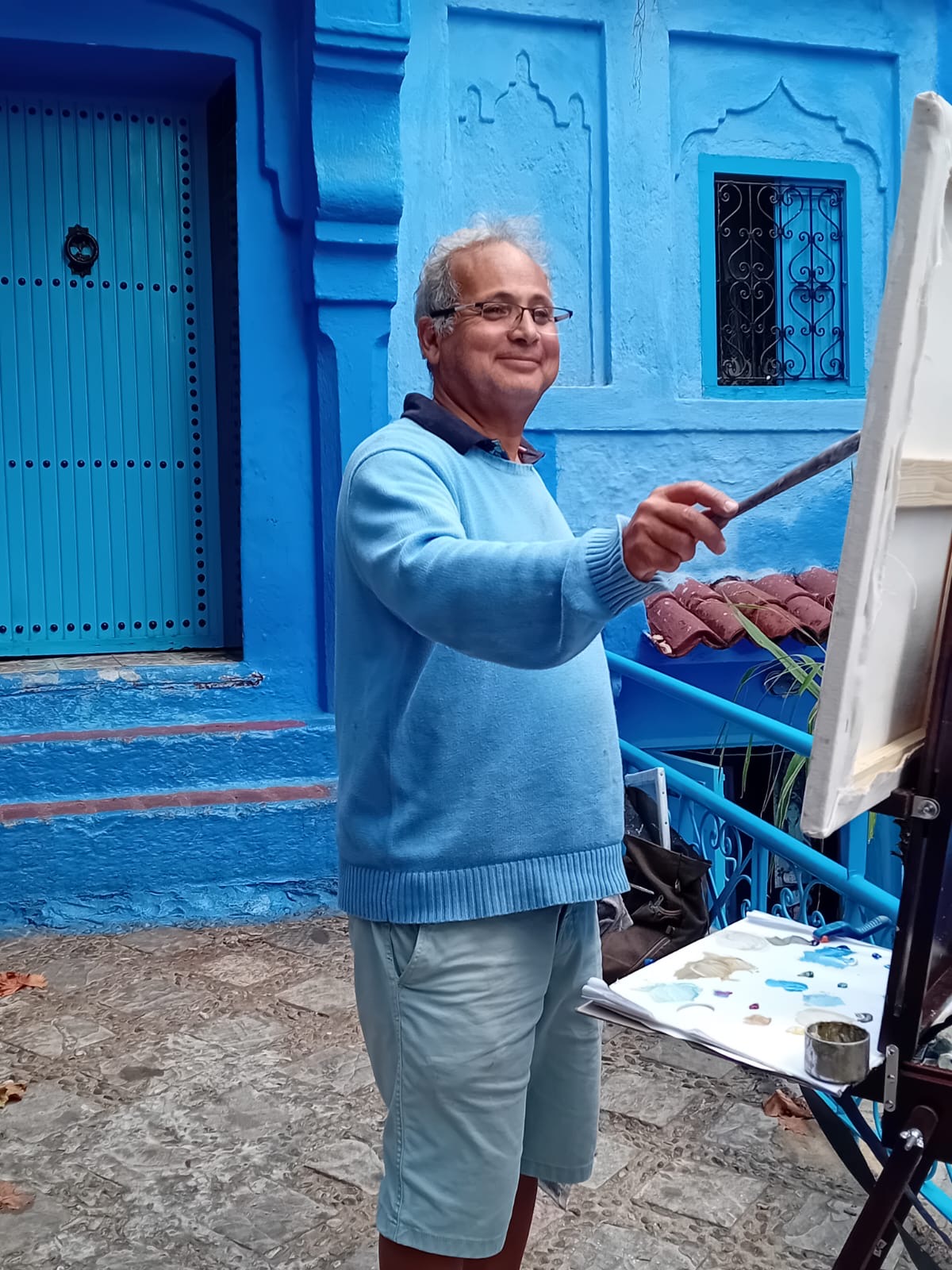 Mohsine peignant devant une façade bleue de Chefchaouen